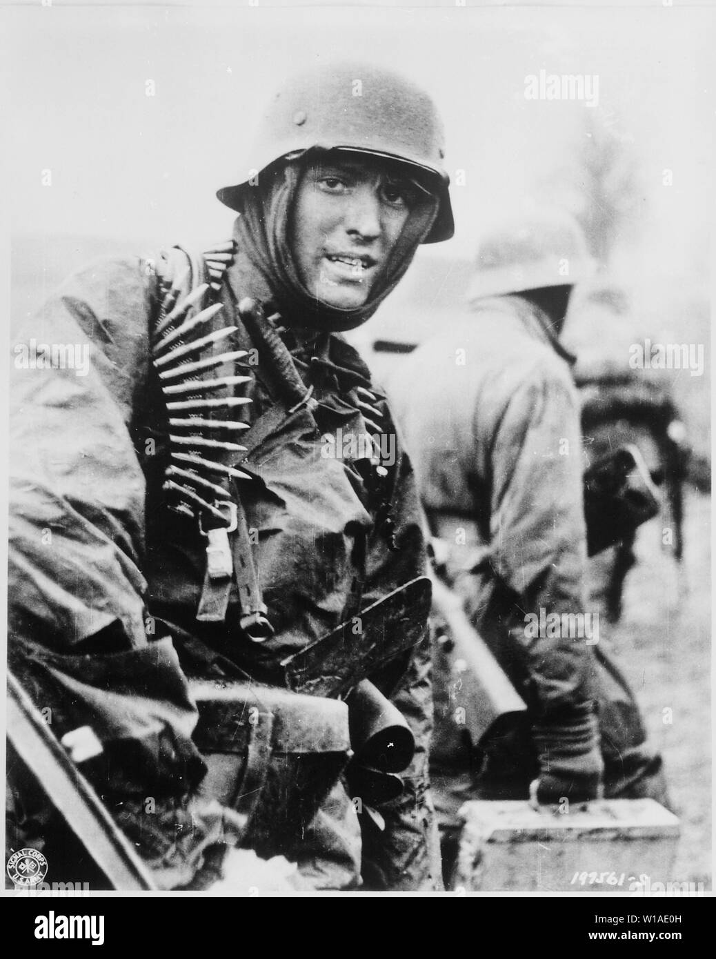 A German Waffen-SS soldier, heavily armed, carries ammunition boxes forward with companion in territory taken by their counter-offensive in this scene from captured German film. Belgium.; General notes:  Use War and Conflict Number 1070 when ordering a reproduction or requesting information about this image. Stock Photo