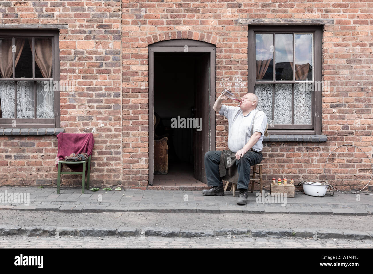 Older man sitting ouside a terraced house, Black Country Living Museum, Dudley UK Stock Photo