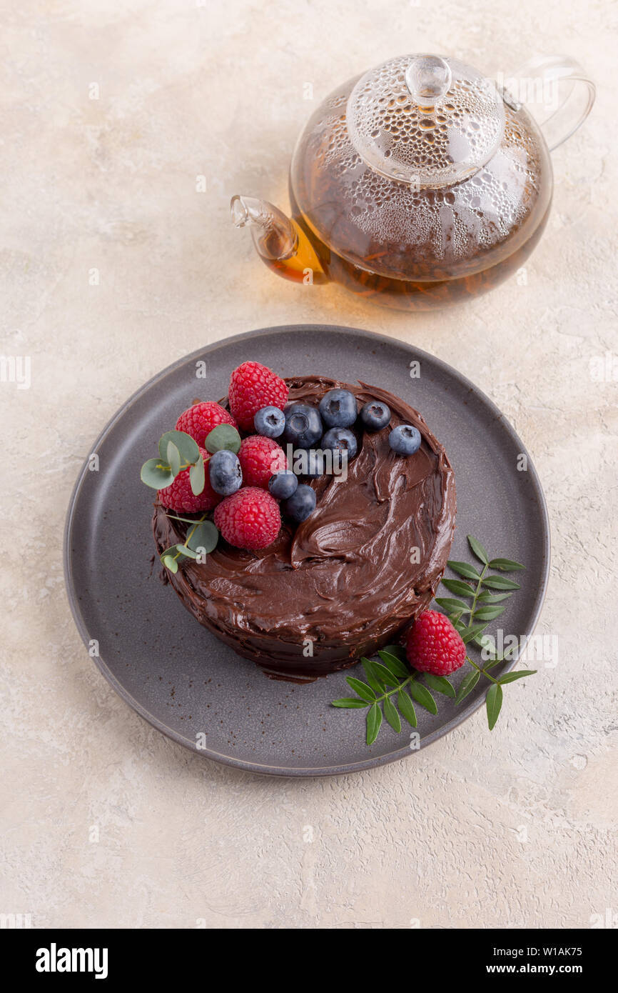 Sweet chocolate cake with berries decor on gray plate with teapot with tea on bright background. Concept of sweet holiday food Stock Photo