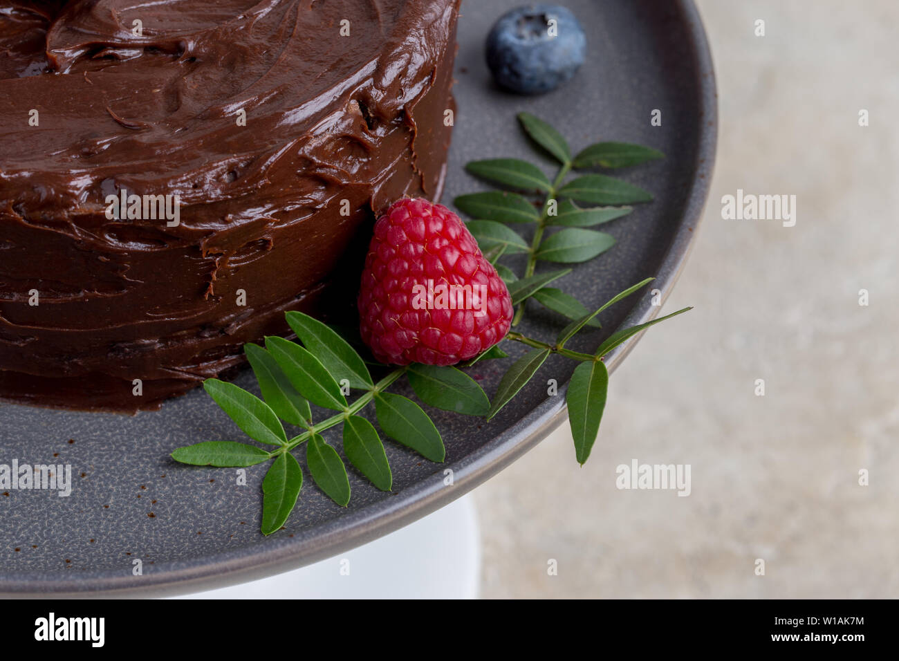 Macro chocolate cake with raspberries and leafs decor at gray plate. Stock Photo