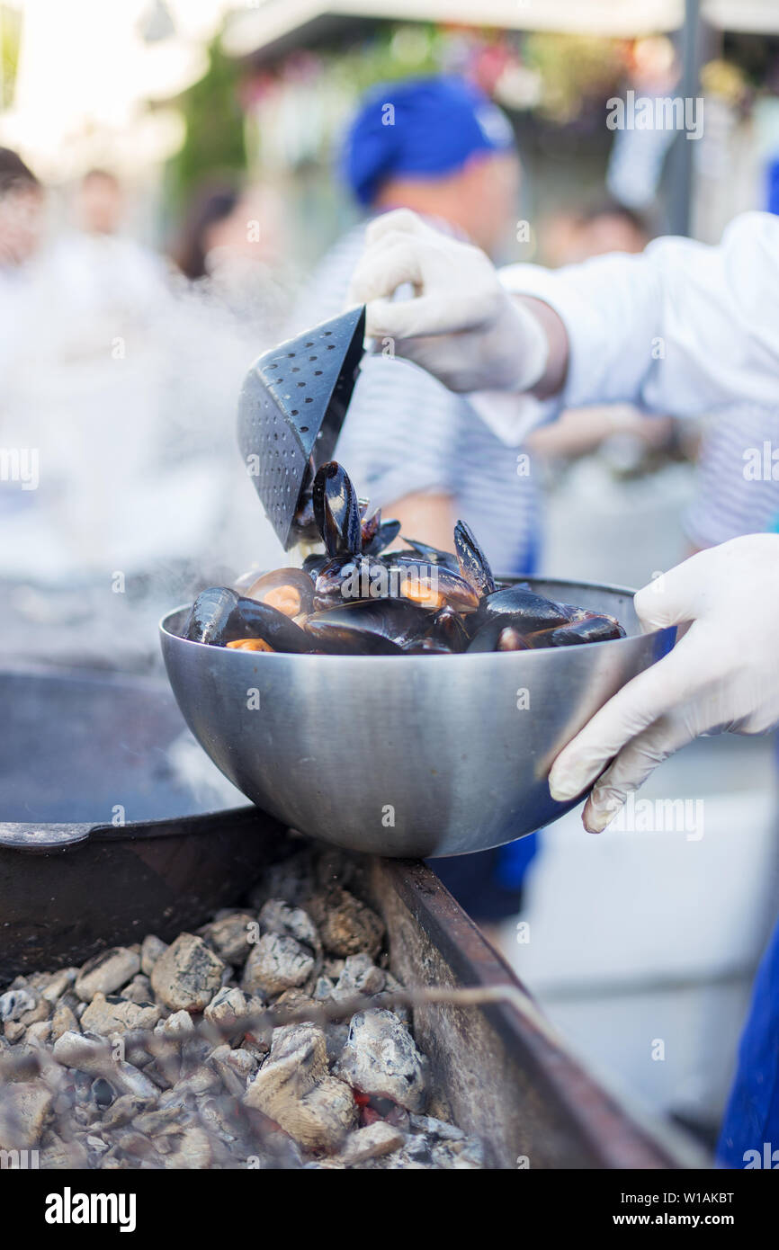 Men's hand cook fresh mussels on open fire. Concept of street food festival Stock Photo