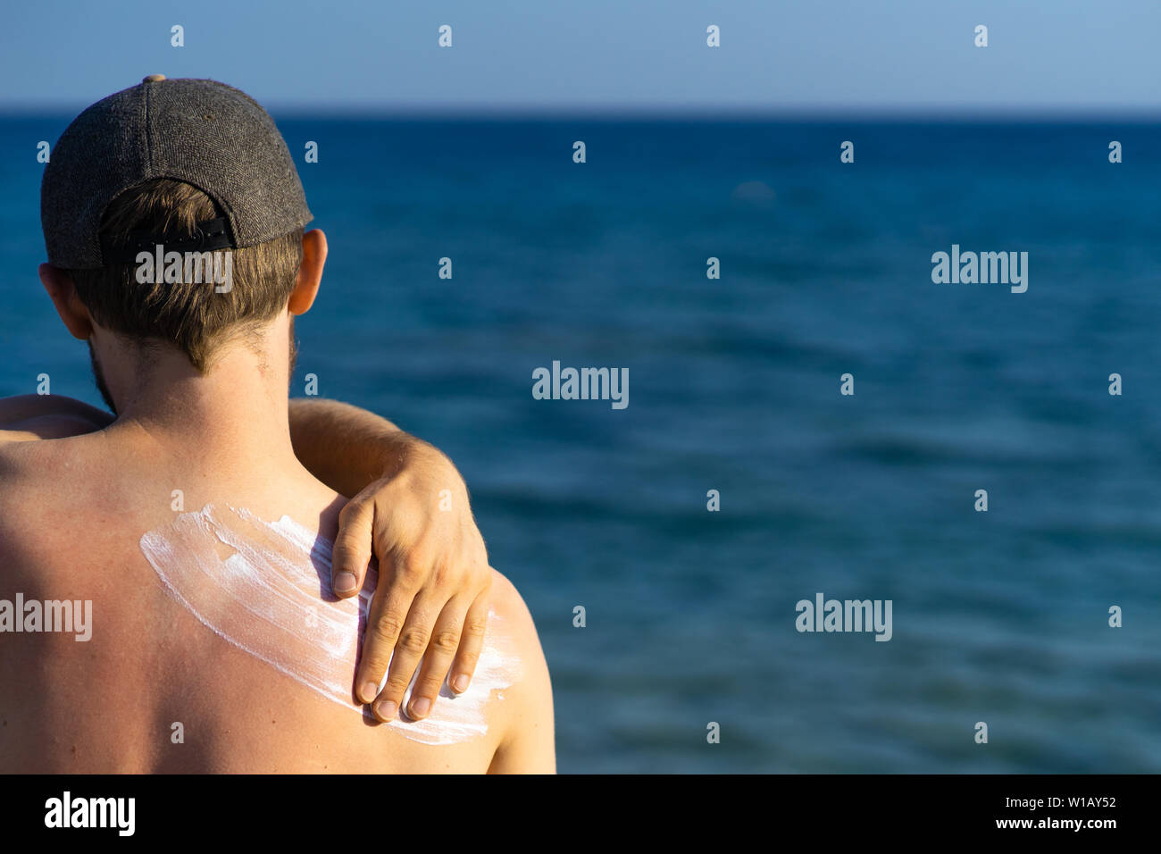 young man with wave-formed suncream on his shoulder standing at the beach, looking over the sea Stock Photo