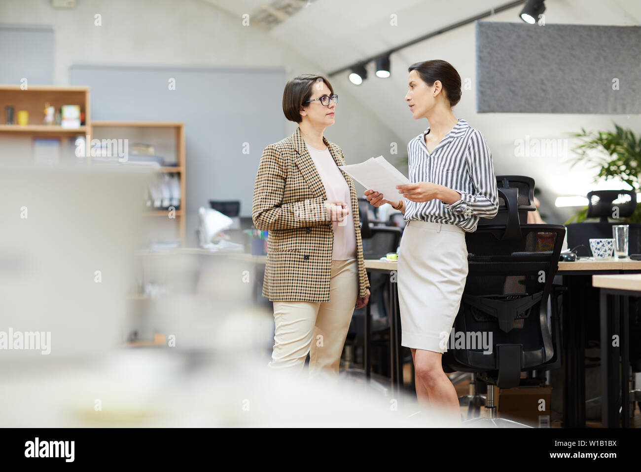 Side view portrait of two contemporary businesswomen discussing work plans while standing in office, copy space Stock Photo