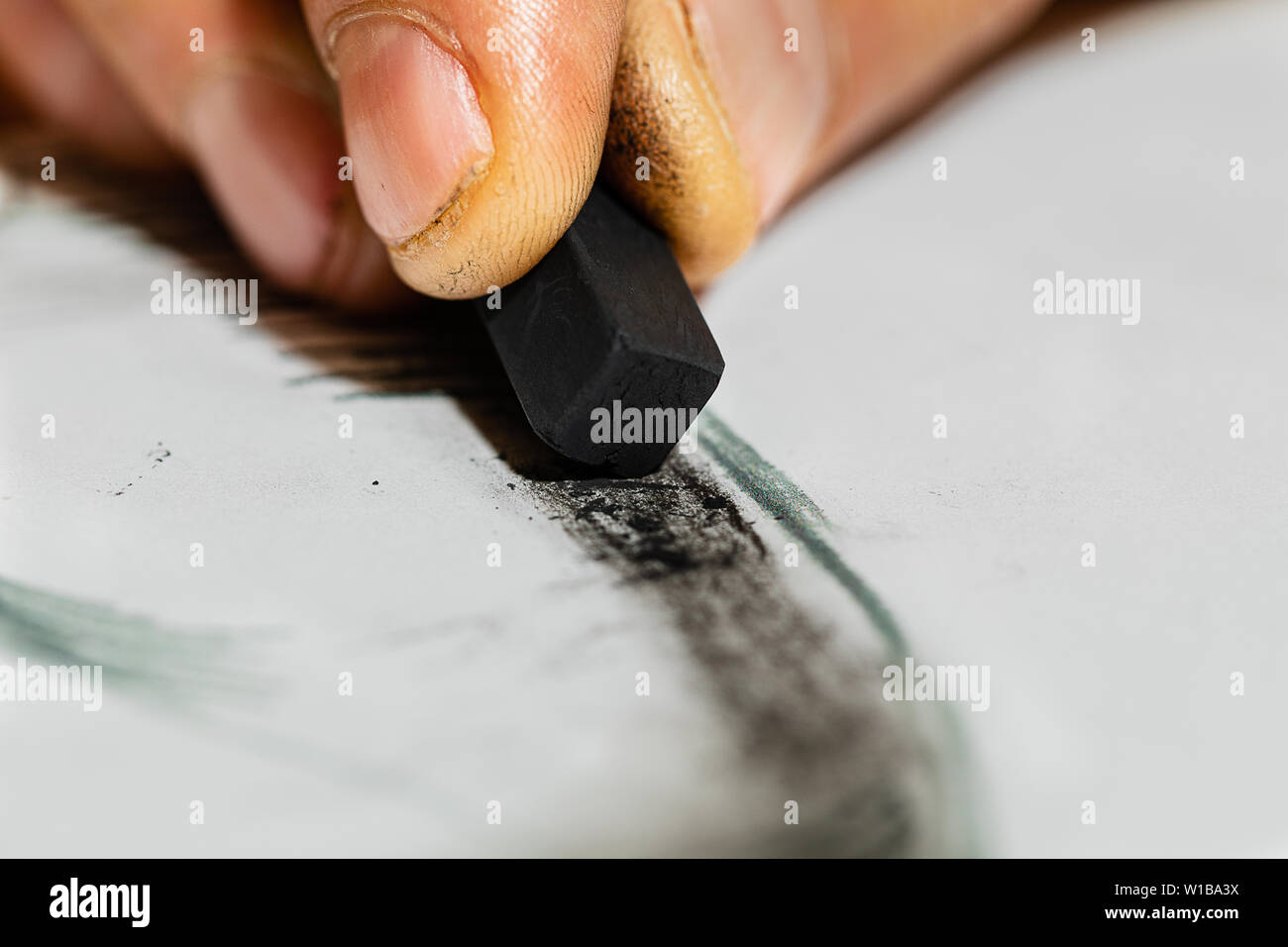 A Macro image of an artist's hand holding a charcoal and shading a picture.  Detail on the hand and the Charcoal is very high and DOF is deep for a ma Stock Photo