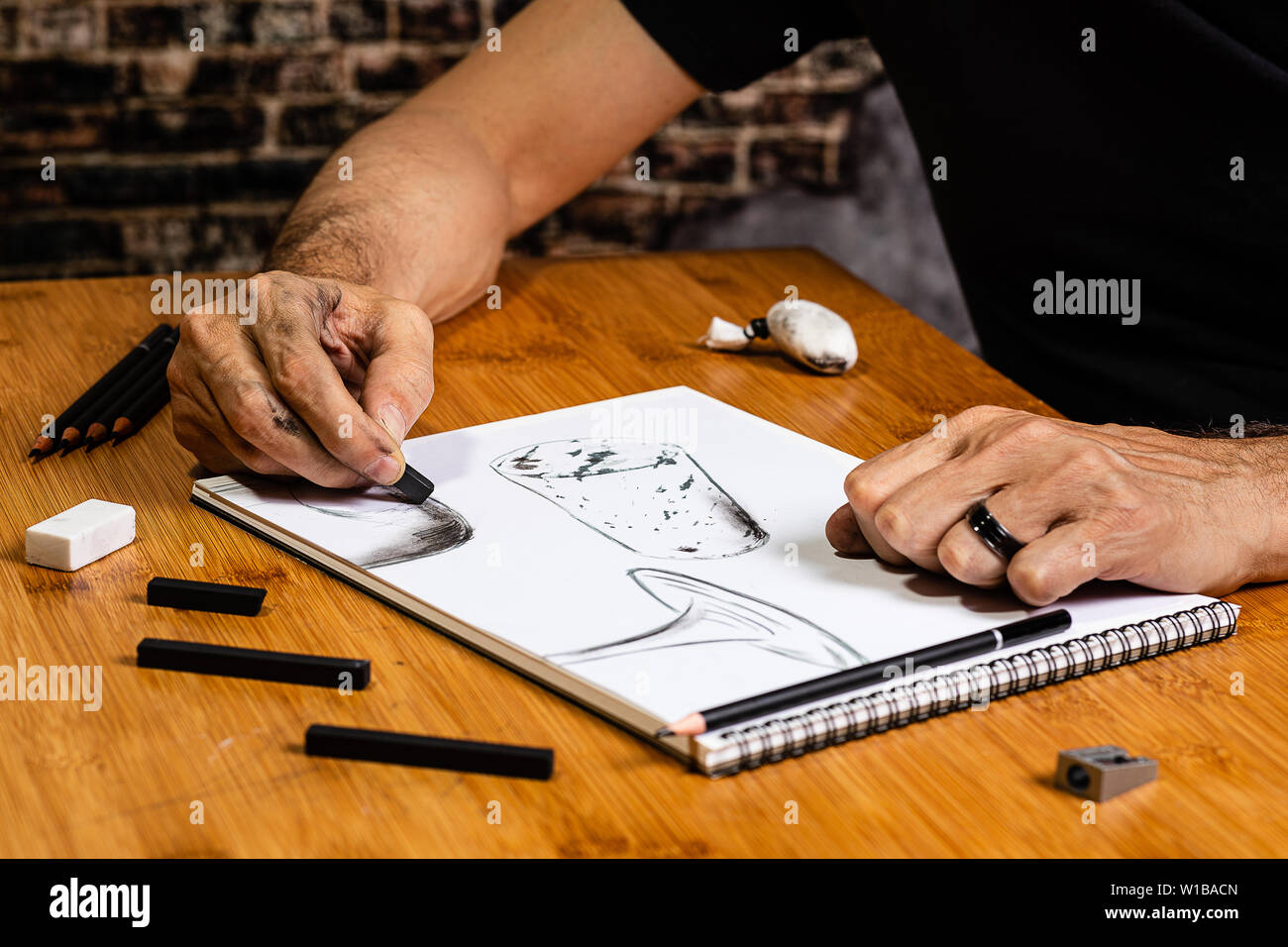 An Artist Sketching a wine bottle, wine glass and a cork at a work table in their studio using pencils and charcoals. Stock Photo