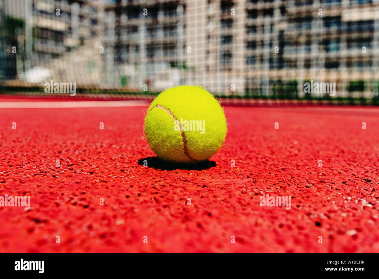 Yellow tennis ball on the red cement court to the sun, summer sports