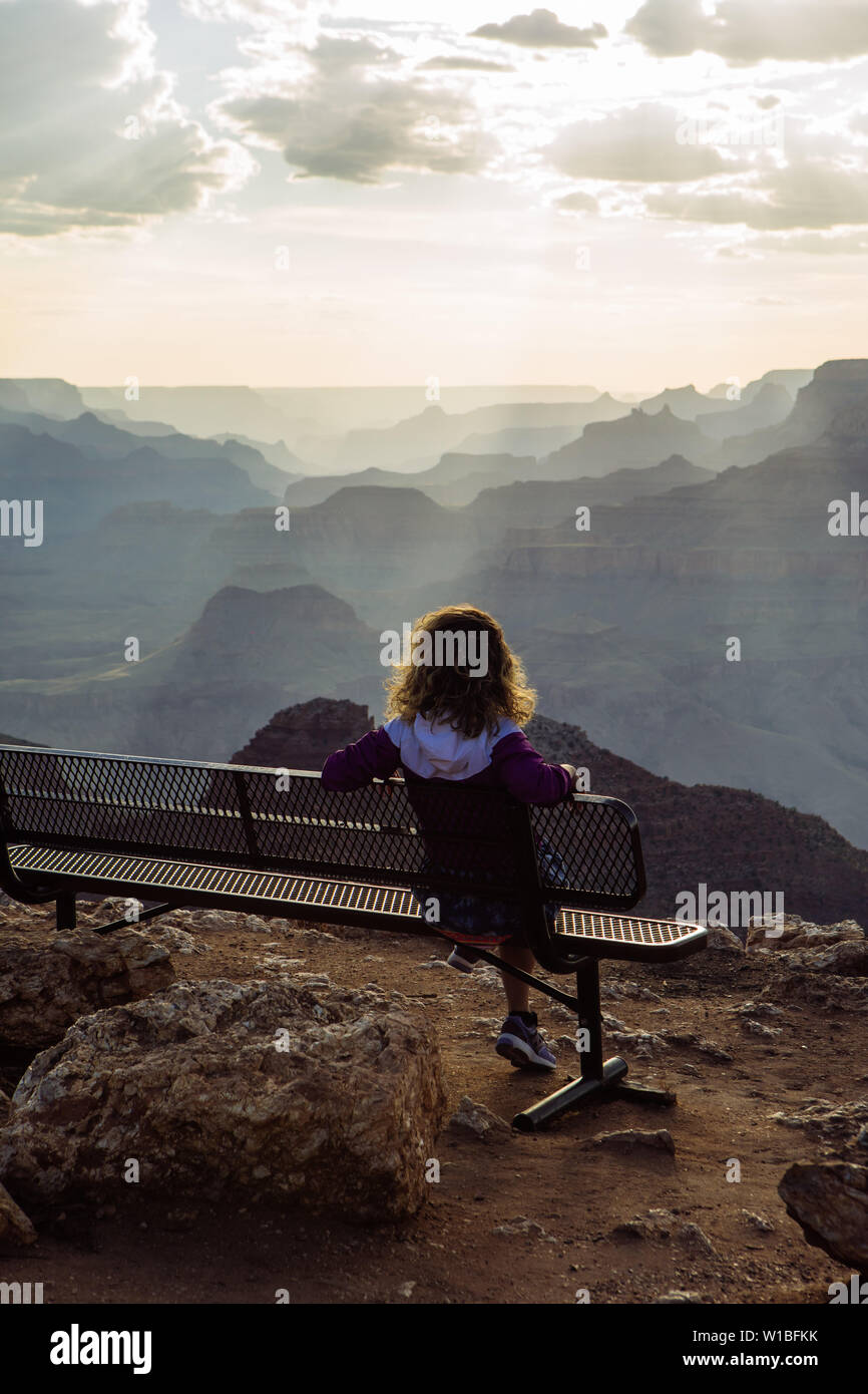 Back Caucasian, curly haired tourist woman watching sunset from a bench in Desert View, Grand Canyon National Park, Arizona, USA Stock Photo