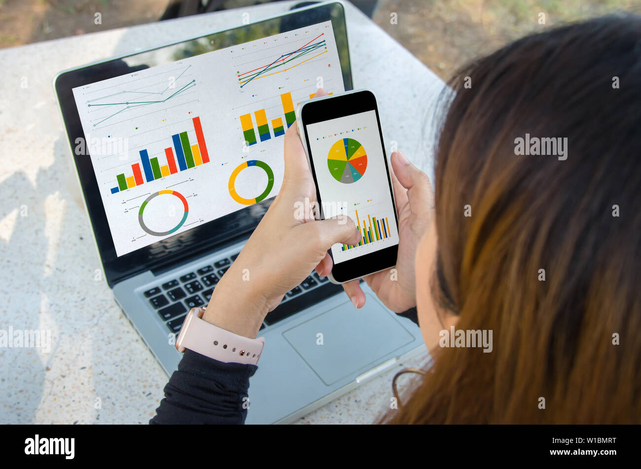 businesswoman working sitting outdoors laptop and smartphone with graphs, diagrams and charts on screen. Stock Photo
