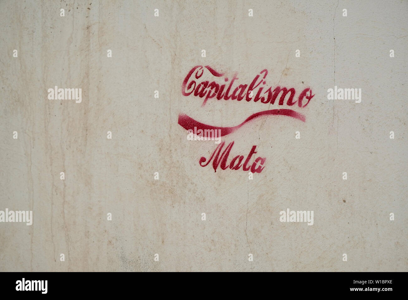 Capitalismo mata (capitalism kills) stencil in red ink and traditional Coca Cola font with wave or dynamic ribbon device on a wall in Granada, Spain. Stock Photo