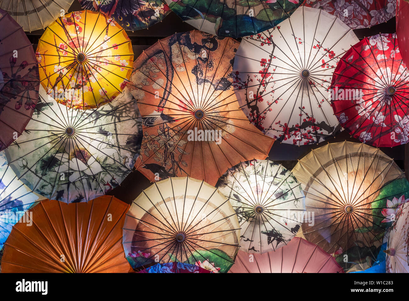 Multi colored chinese umbrellas hanging on a wall illuminated at night Stock Photo