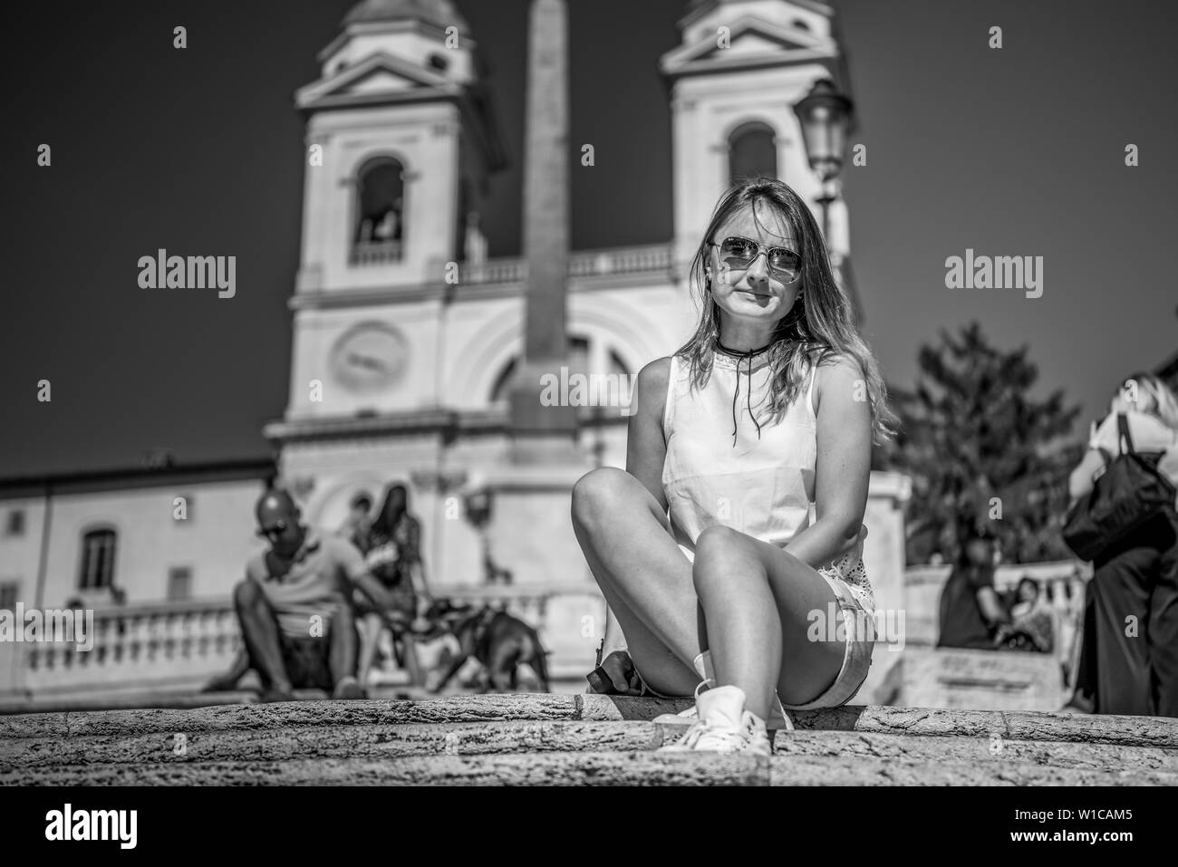 On a sunny summer day, at the base of an incredible building, the woman poses and smiles pale in front of the photo-lens, thus creating memories that Stock Photo