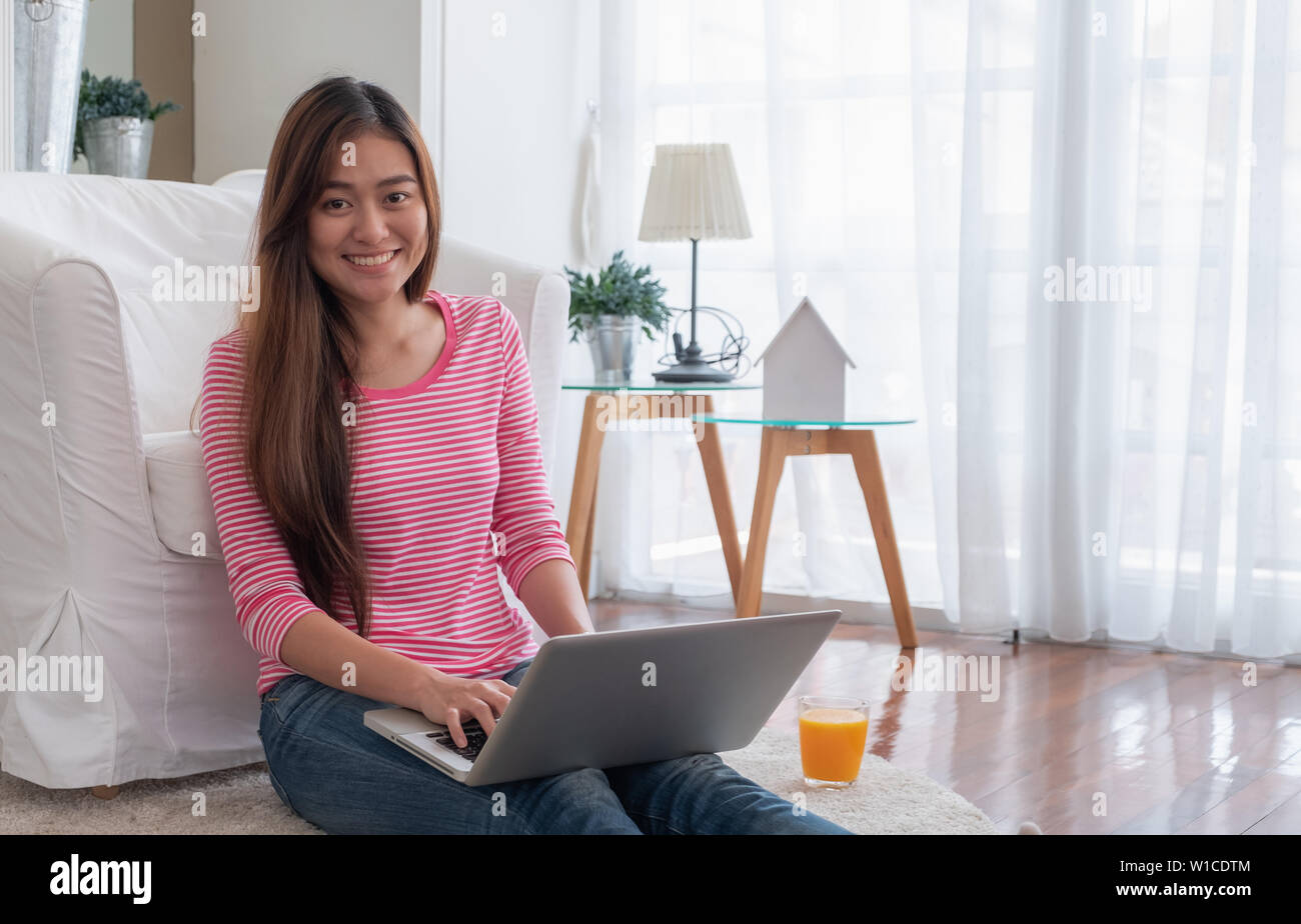 Happy asian woman working on laptop computer at home.female freelancer sitting on carpet on floor work at home in living room. Stock Photo