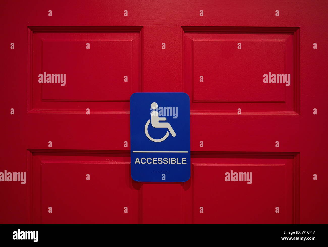 A blue handicap sign or marker mounted on a deep red restroom door. Stock Photo