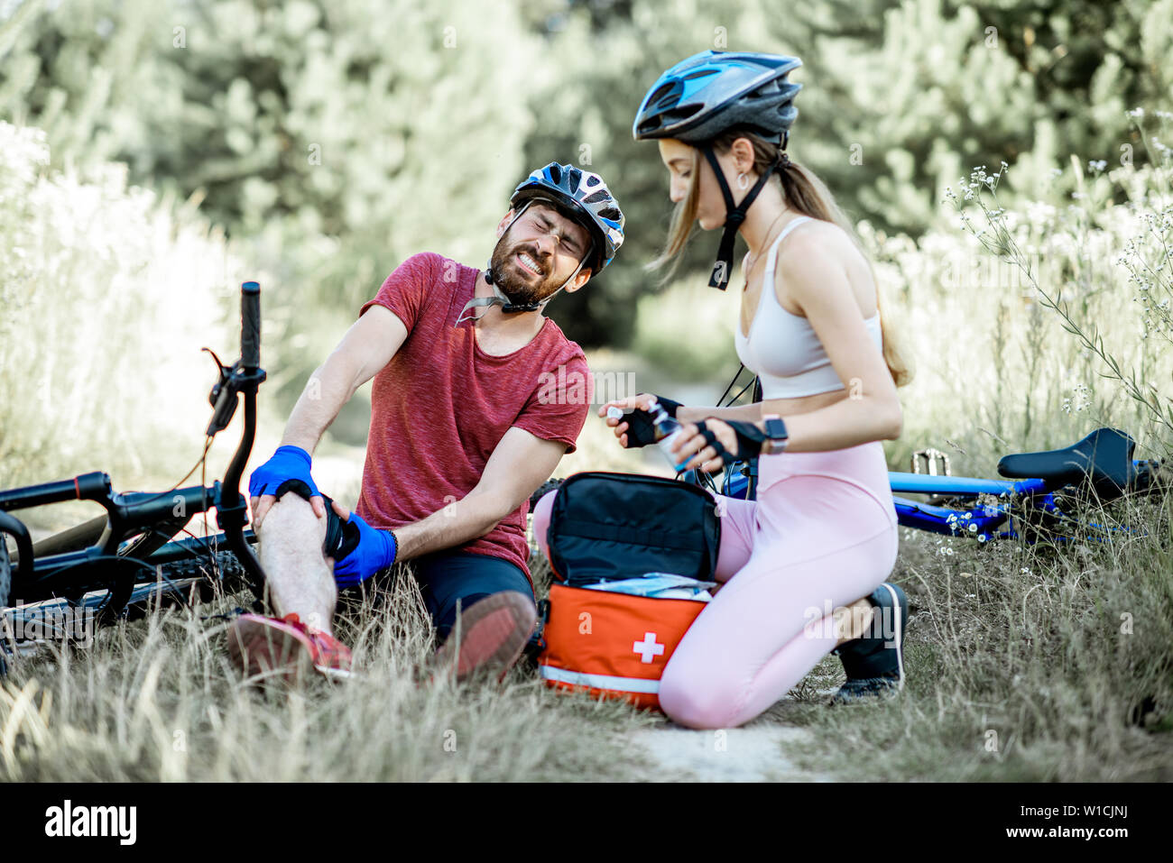 Woman giving first aid to a man with knee injury while cycling on the ...