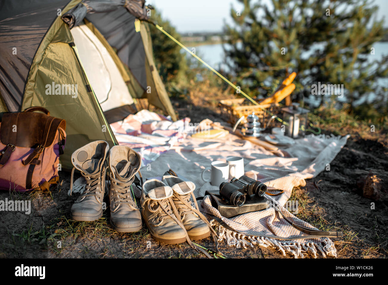 Campsite with tent, trekking shoes, backpack, plaid in the forest Stock
