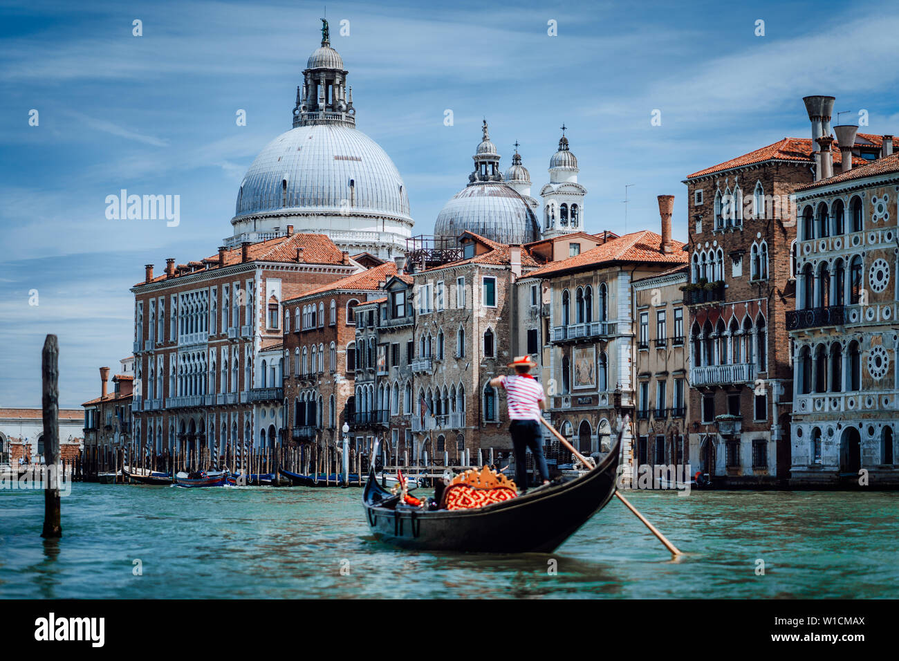 Traditional Gondola and gondolier on Canal Grande with Basilica di Santa Maria della Salute in the background in Venice, Italy. Summer vacation city Stock Photo