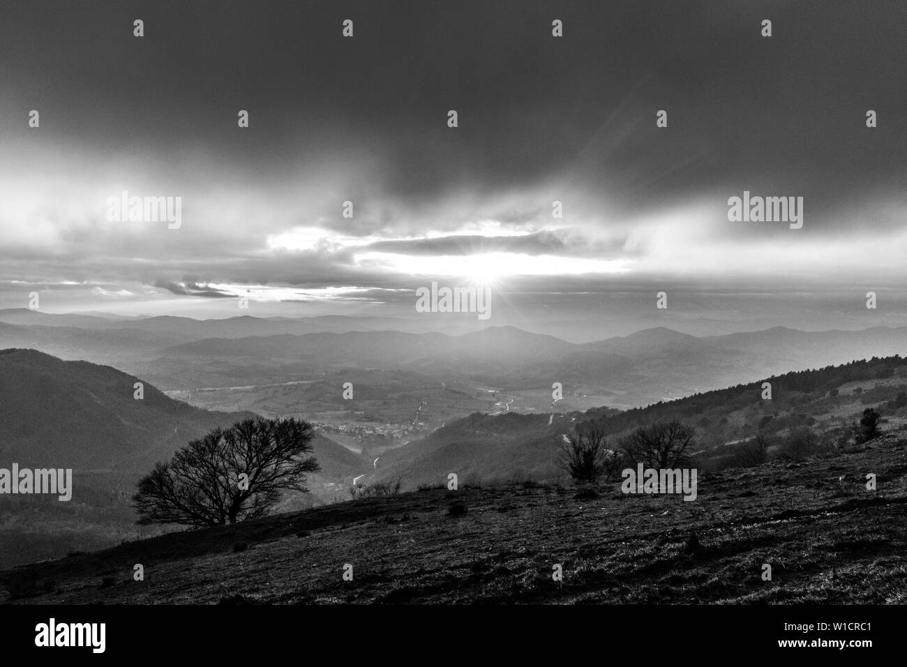 Moody sunset on Monte Cucco (Umbria, Italy), with tree in the foreground and sun filtering through clouds Stock Photo
