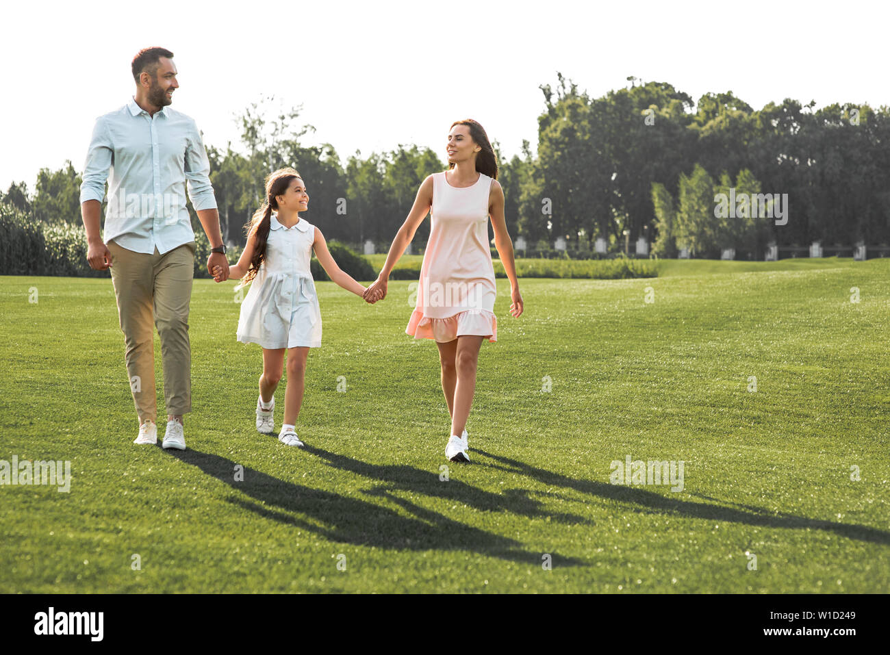 Enjoying time together. Full length of happy and young family of three holding hands, smiling and walking outdoors. Concept of a happy family. Picnic. Weekend Stock Photo
