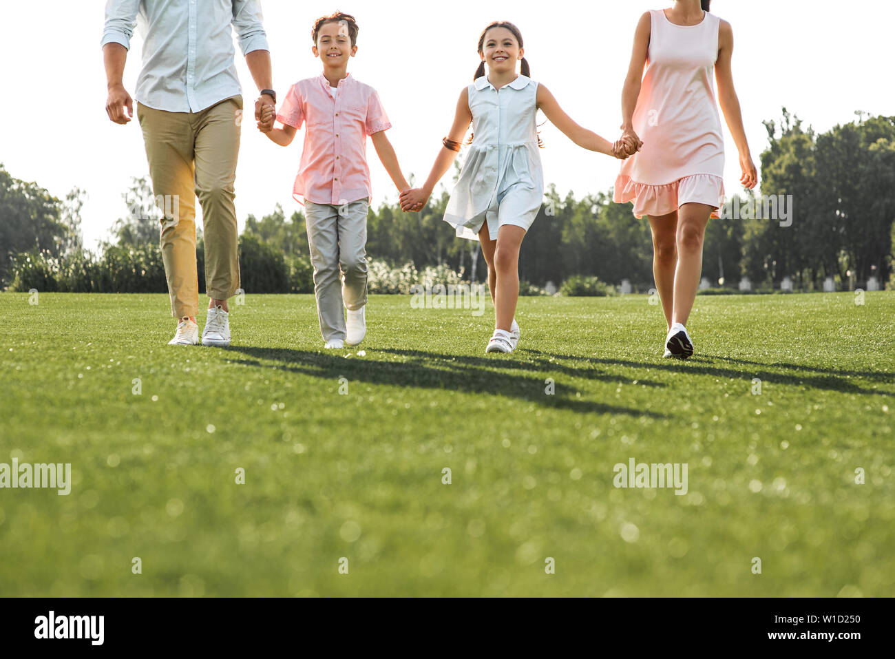 Happy moments. Full length of positive and young family of four holding hands, smiling and walking outdoors. Picnic. Weekend Stock Photo