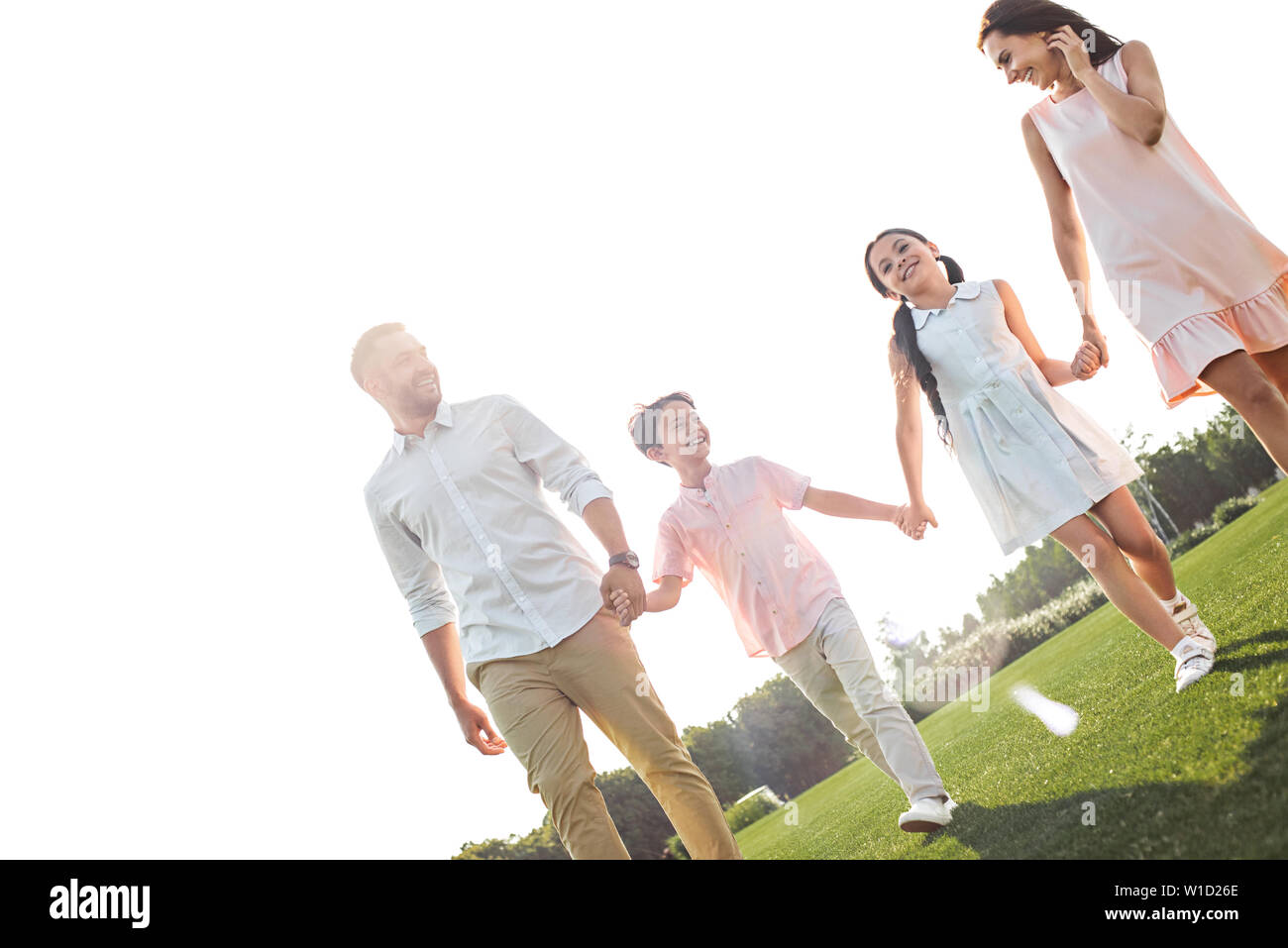 Happy to be a family. Full length of young and positive family of four holding hands, smiling and spending time together outdoors. Picnic. Weekend Stock Photo