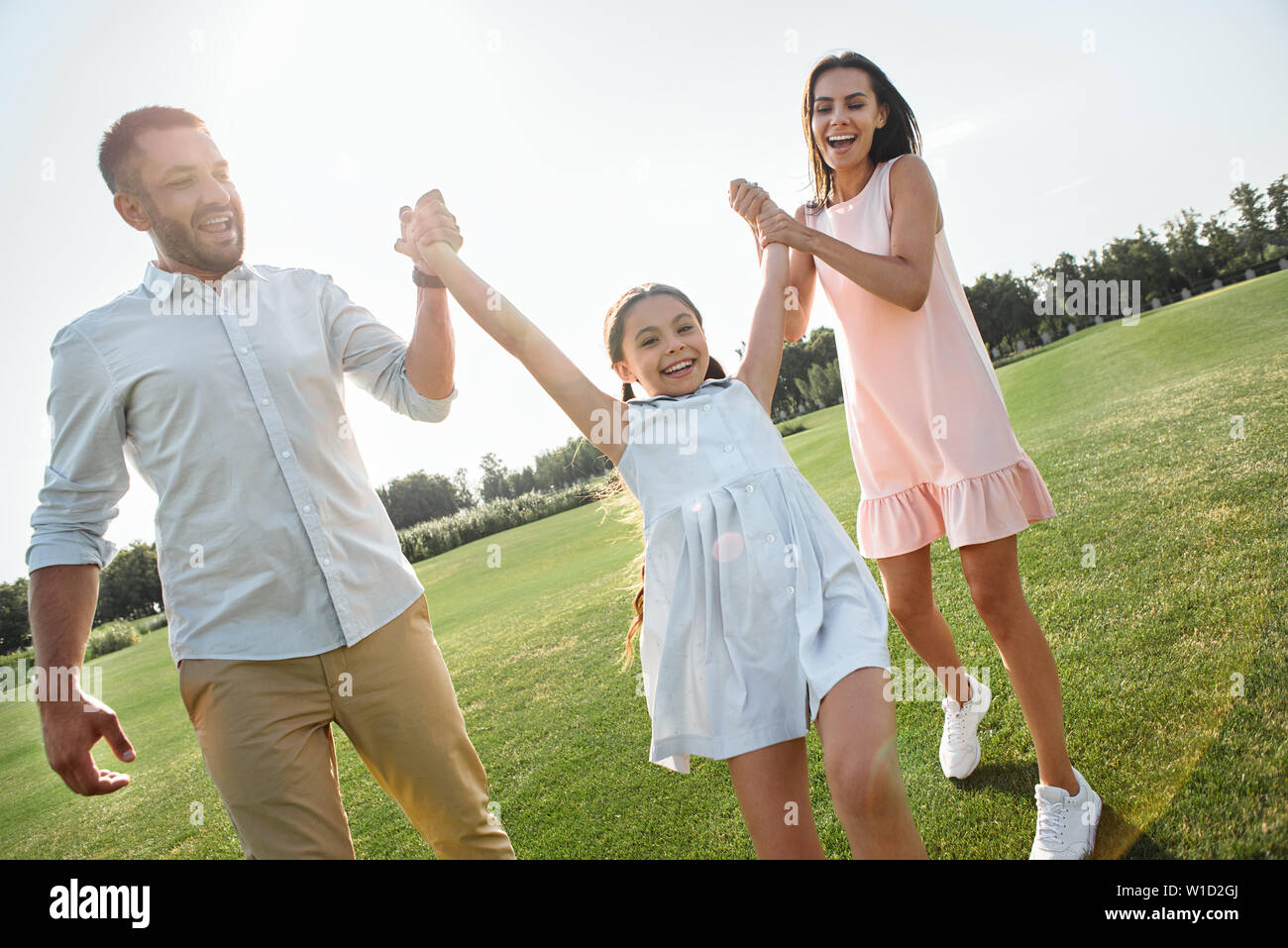 Let's play Full length of young and happy parents carrying their daughter and smiling while spending time together outdoors. Family concept Stock Photo