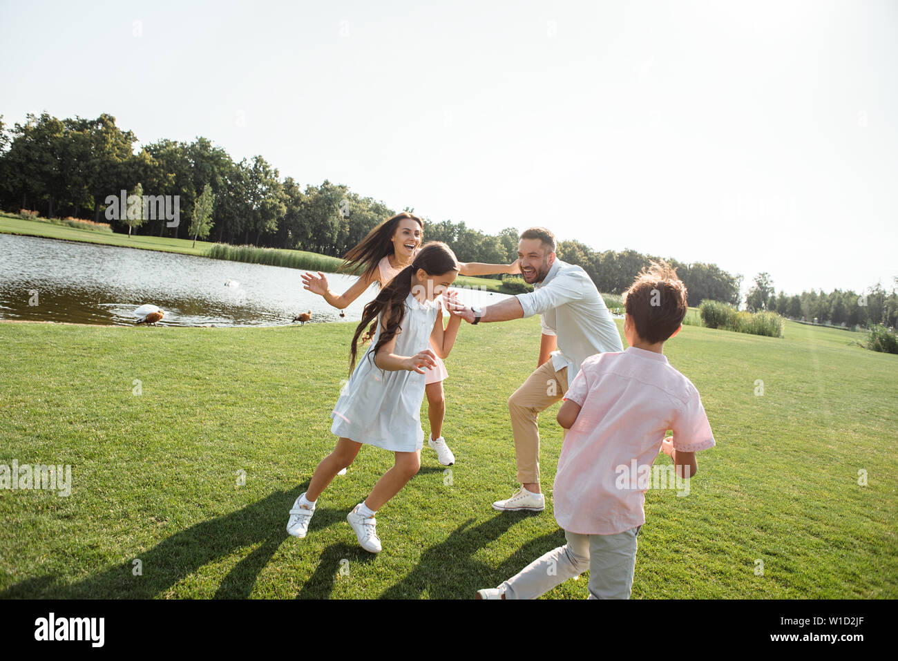 Try to catch me Happy young family playing and smiling while spending free time with family outdoors in park. Family concept Stock Photo