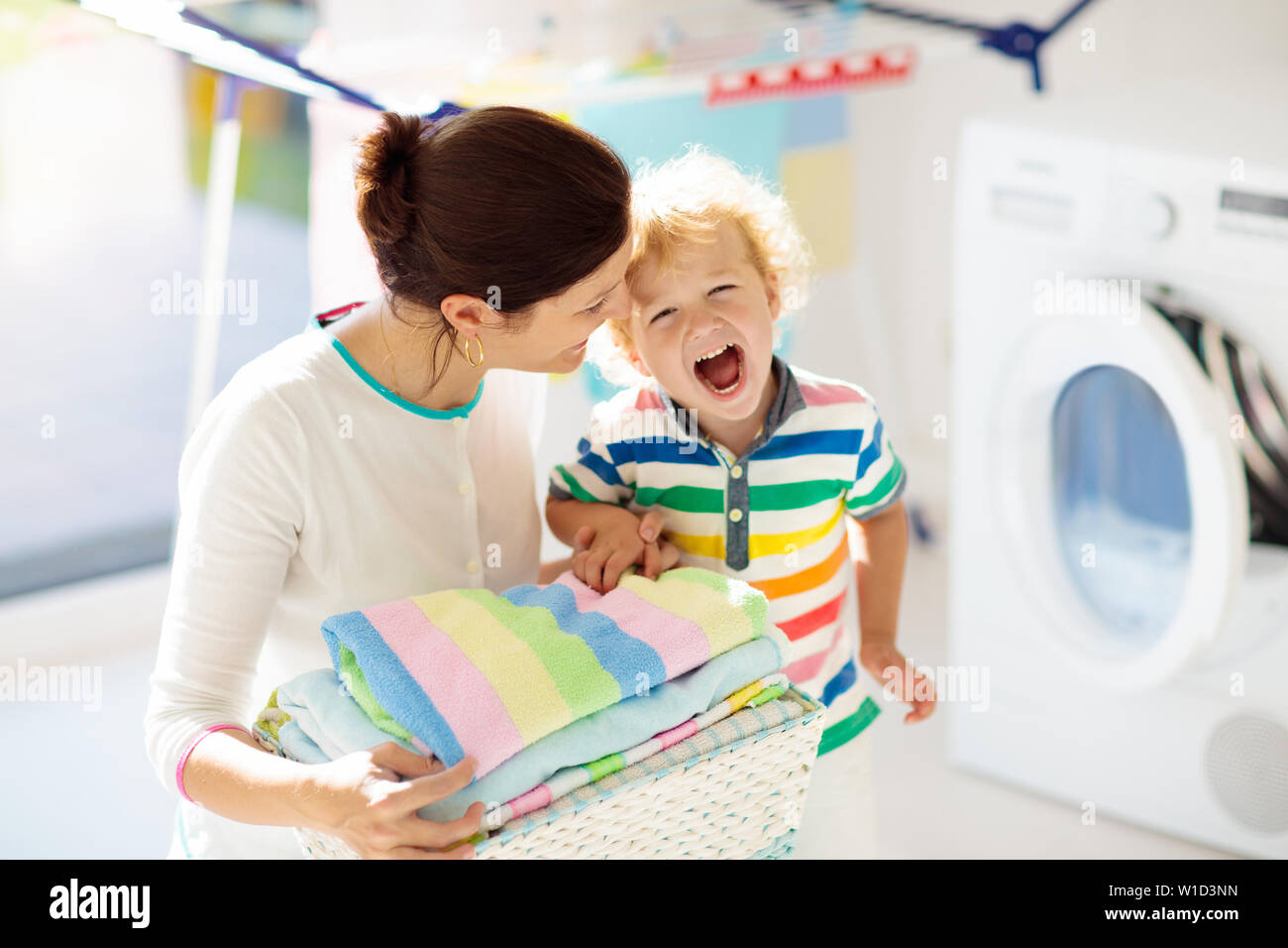Mother and kids in laundry room with washing machine or tumble dryer. Family chores. Modern