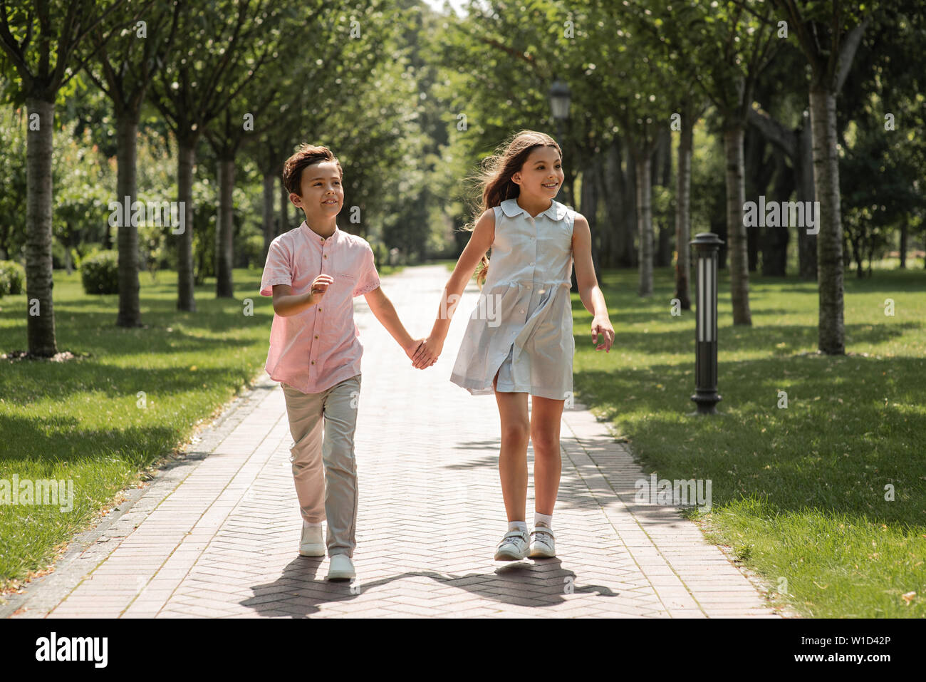First love. Little boy and girl holding hands and smiling while walking ...