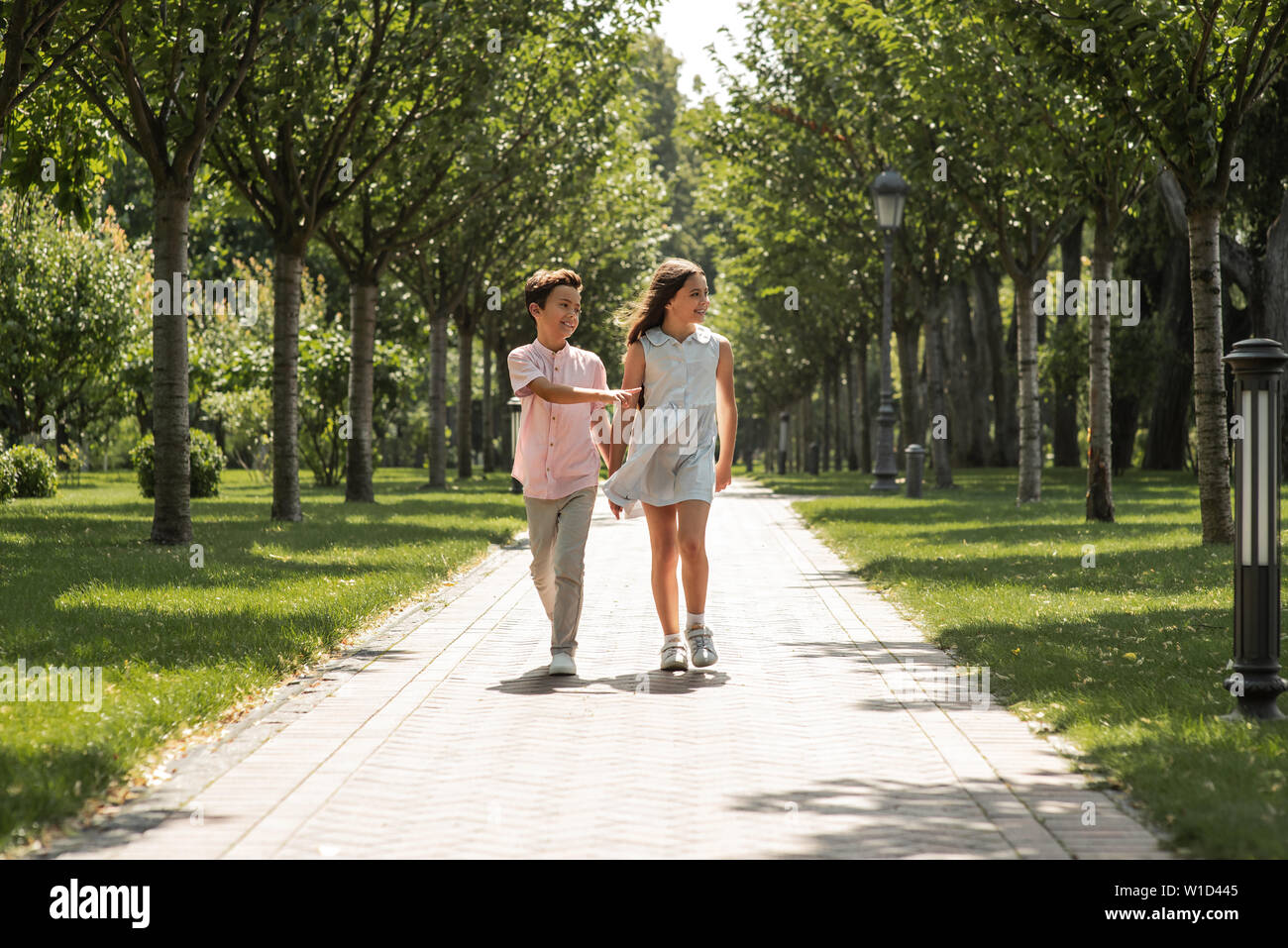 You are my best frind. Little boy and girl holding hands and smiling while walking together in park. Summertime. Friendship Stock Photo