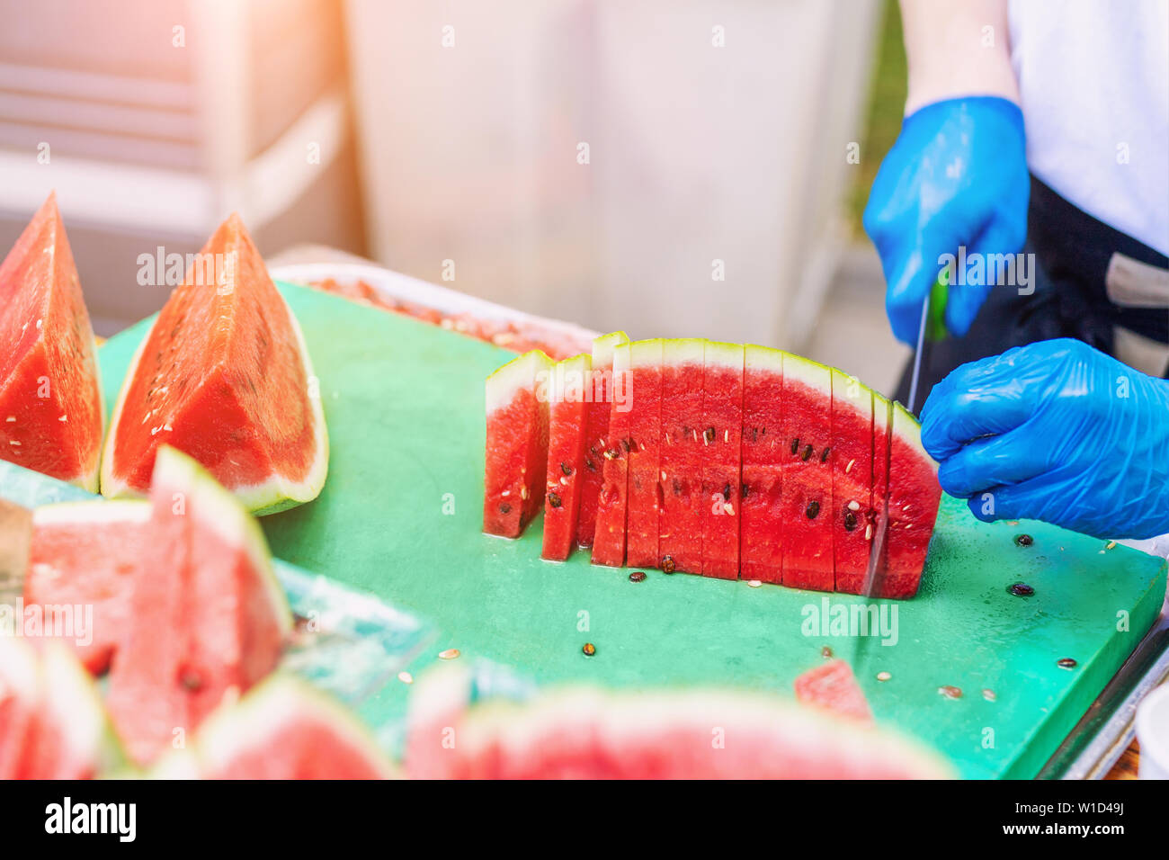 Cook in rubber gloves peeling and slicing gresh tasty juicy sliced watermelon for hotel guests at tropical resort outdoors Stock Photo