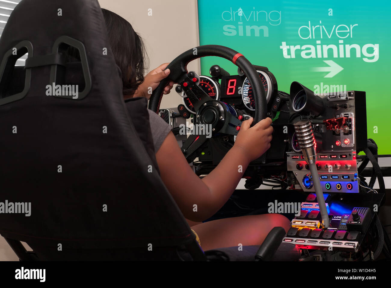 A young person sitting in a racing cockpit and selecting driver training from the gaming screen while holding the steering wheel. Stock Photo