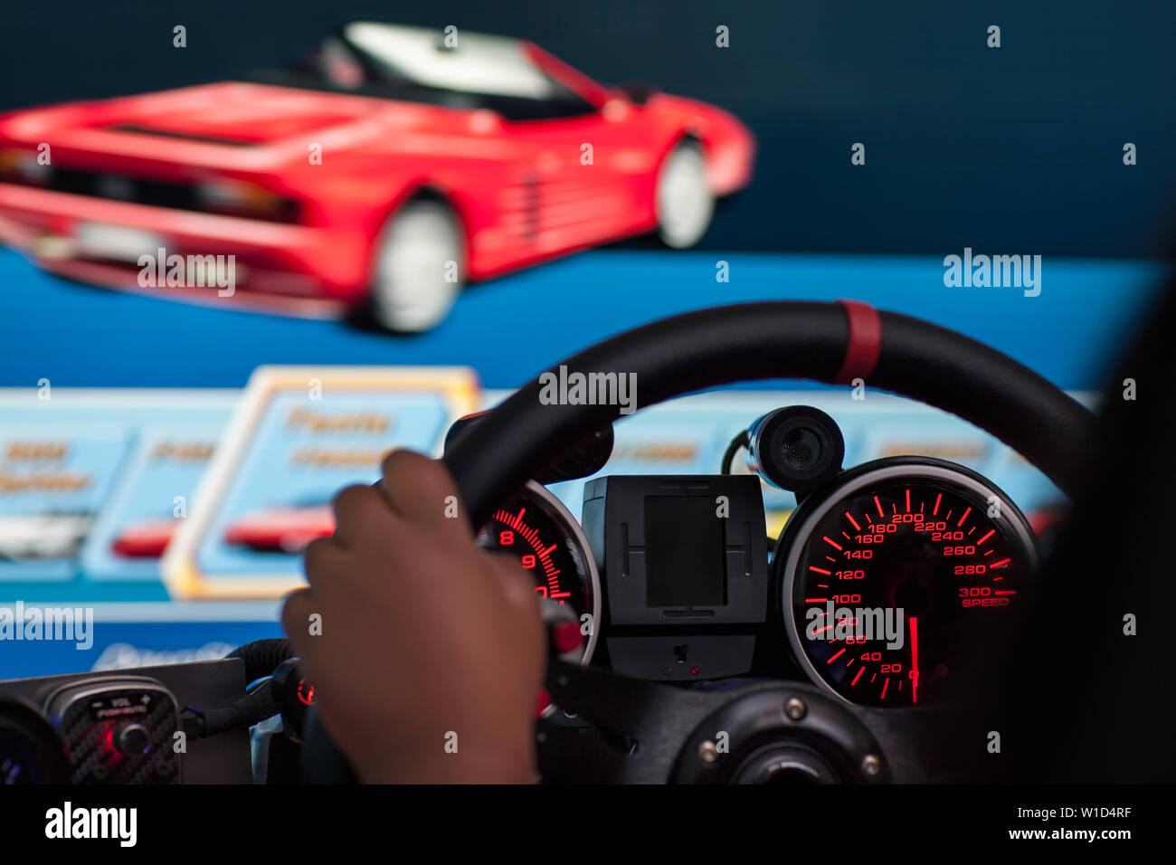 Closeup view of someone playing a retro style arcade racing game on a simulator cockpit with lit gauges. Stock Photo