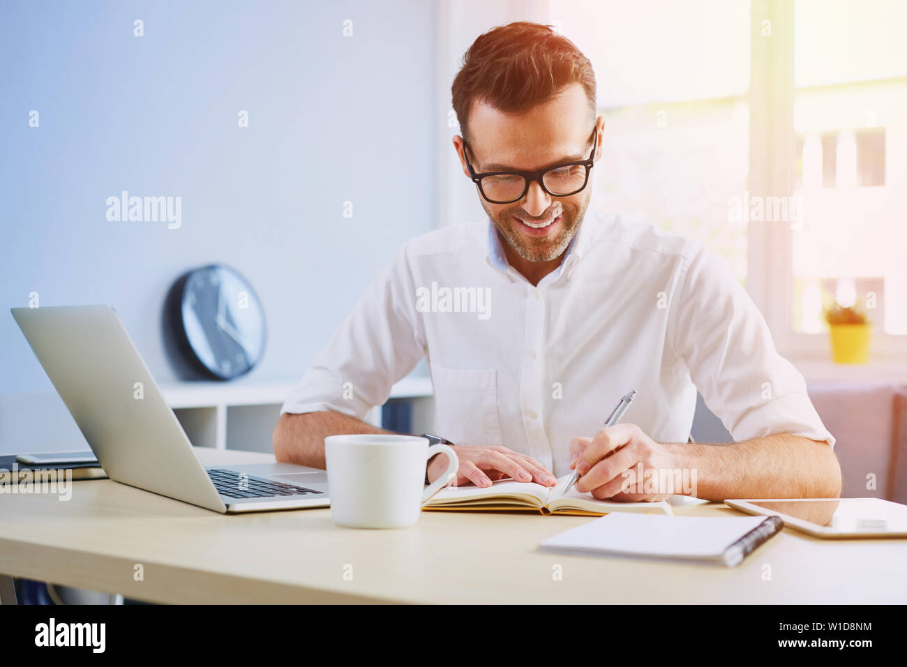 Handsome man working from home office doing notes sitting at desk Stock Photo