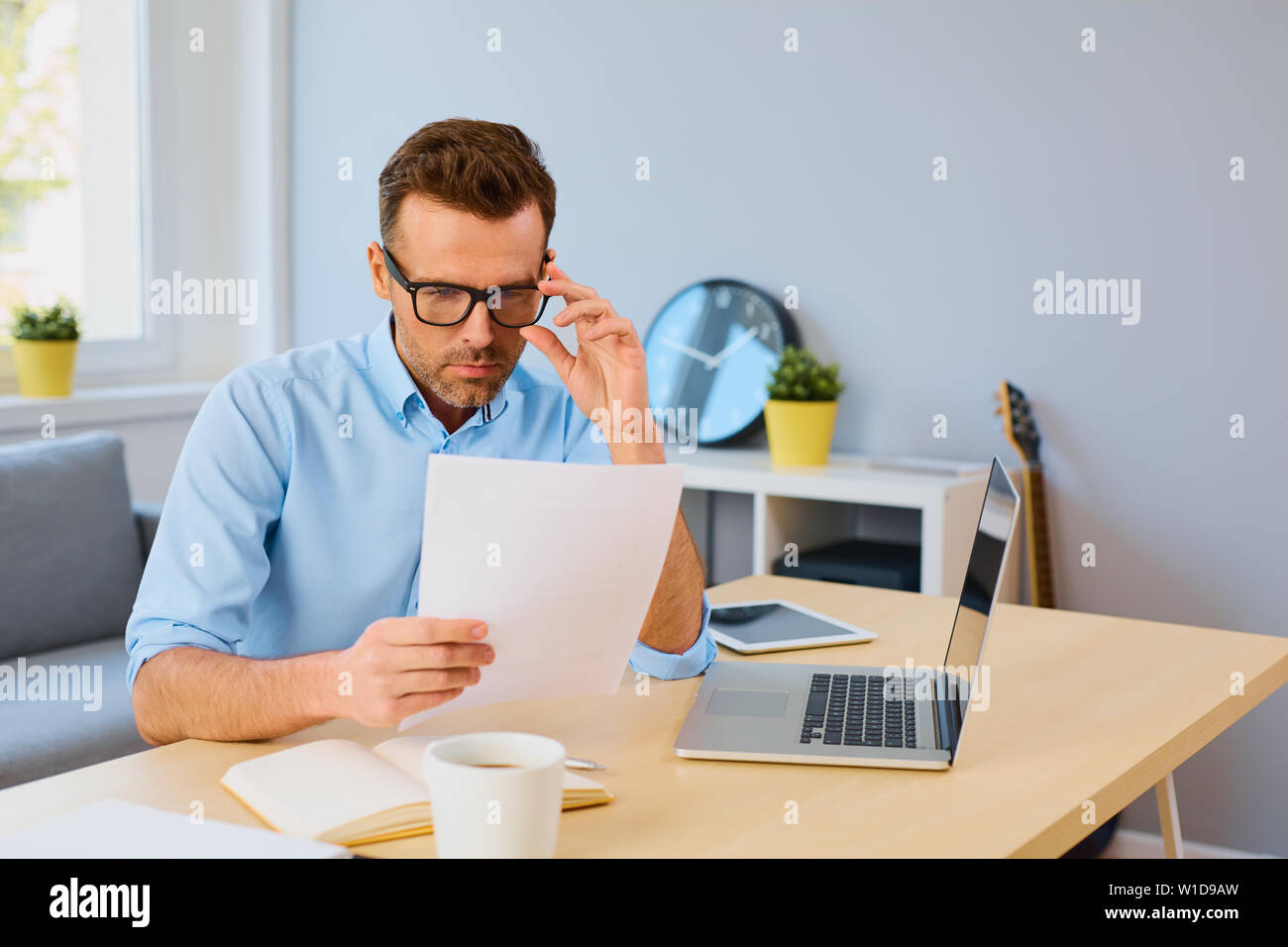 Serious man reading document at home sitting by desk Stock Photo