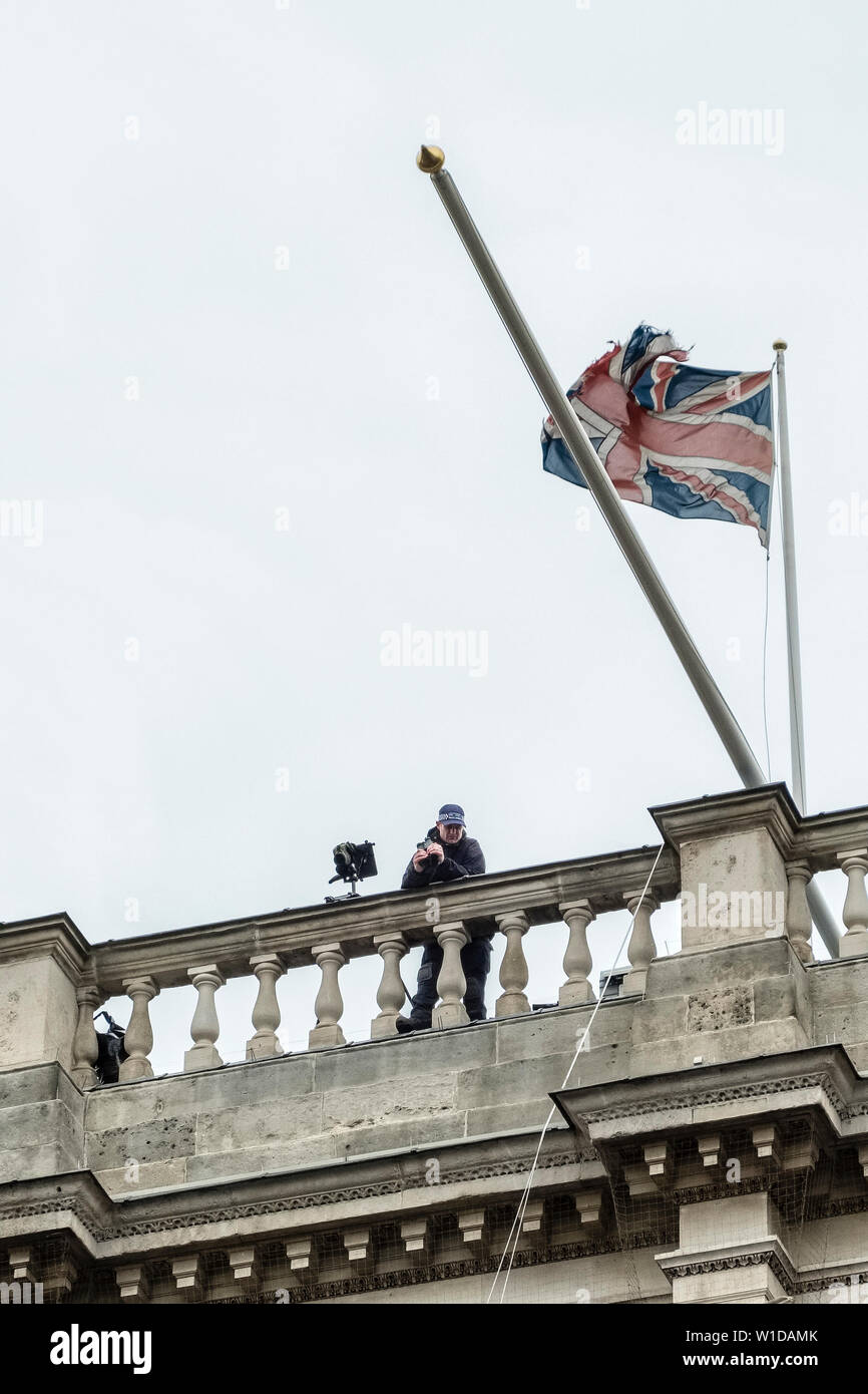 London, UK. High on a rooftop beneath a tattered British flag, a policeman scans a crowd of demonstrators through high-powered binoculars Stock Photo