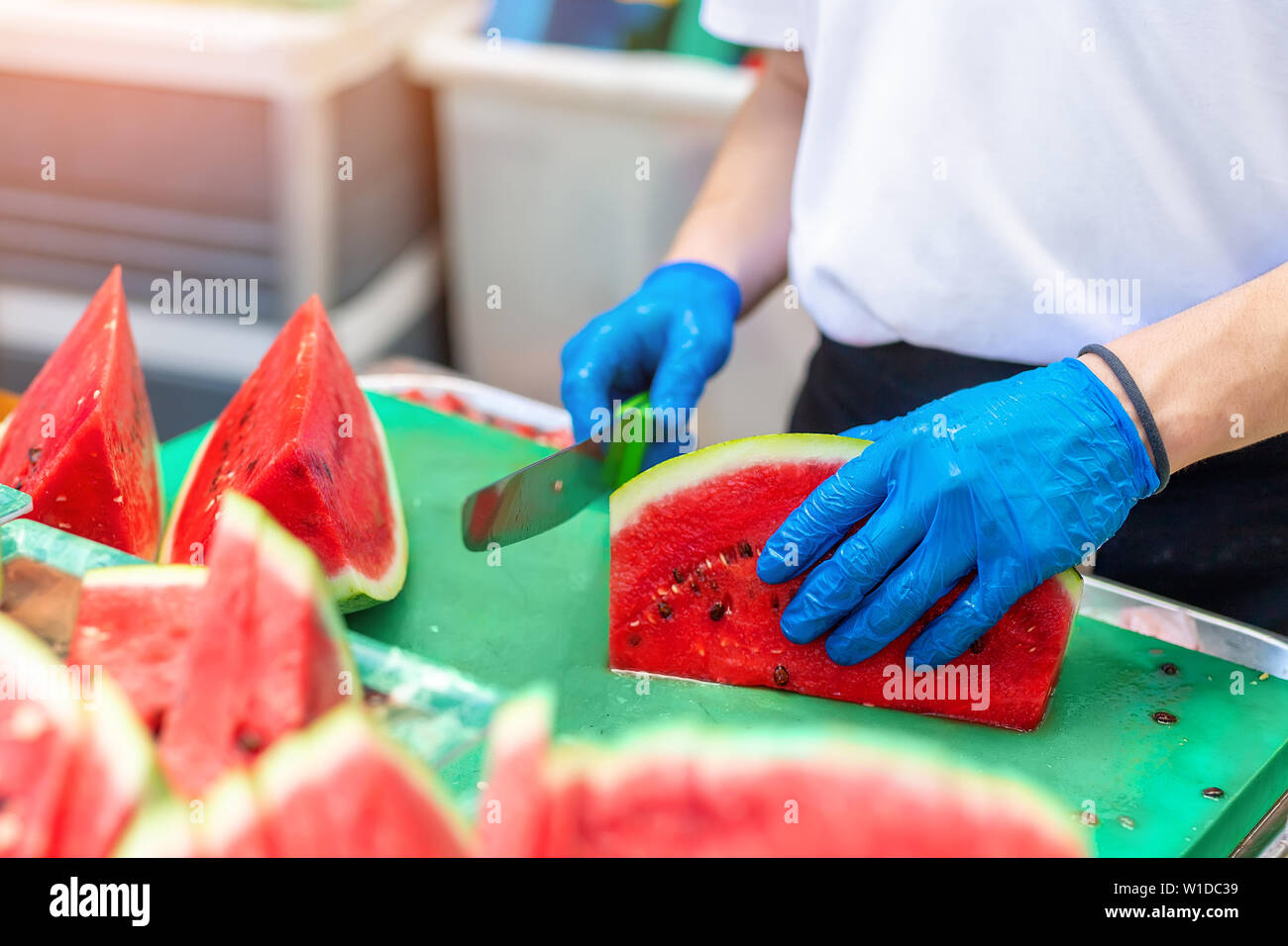 Cook in rubber gloves peeling and slicing gresh tasty juicy sliced watermelon for hotel guests at tropical resort outdoors Stock Photo