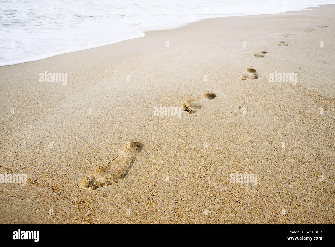 Summer background. Footprints on a sandy beach. Sea Wave Foam in the Sand Stock Photo