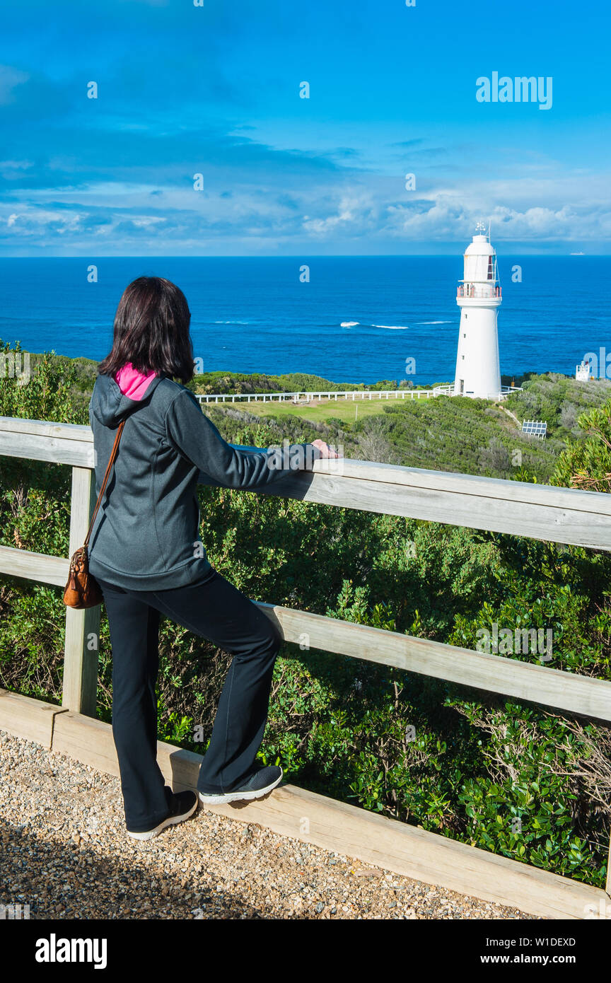 View of Cape Otway Lighthouse in Victoria, Australia as a female tourist enjoys the spectacular scene of the Southern Ocean behind the guard rails Stock Photo