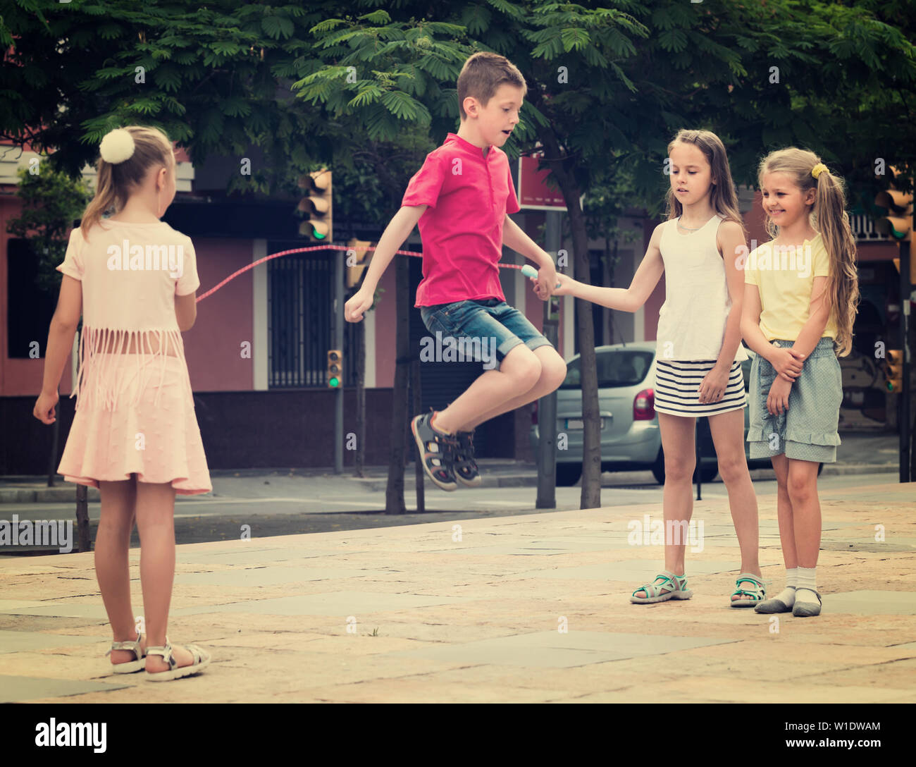 group of smiling children skipping together with jumping rope on urban ...