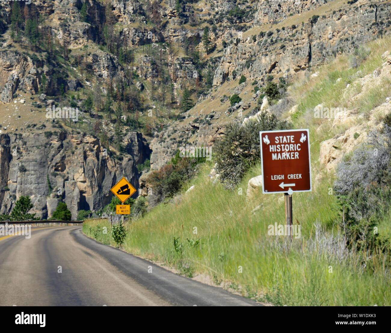 Roadside signs of a state historic marker and warning of sloping road