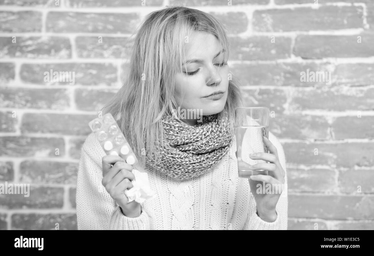 Taking cold medicine. Ill woman treating symptoms caused by cold or flu. Medication and increased fluid intake. Unhealthy woman holding pills and water glass. Cute sick girl taking anti cold pills. Stock Photo