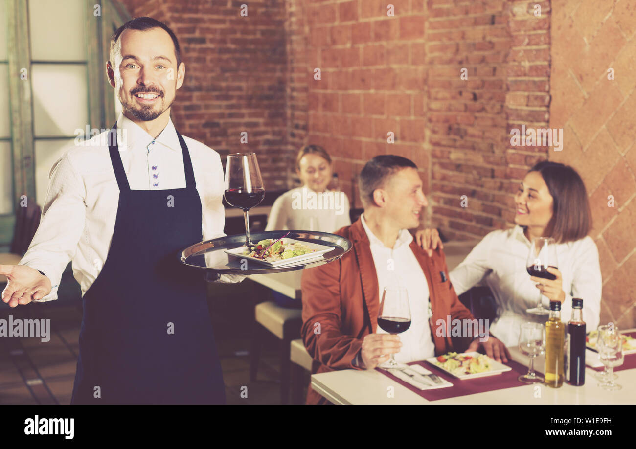 Nice male waiter showing country restaurant to visitors Stock Photo - Alamy