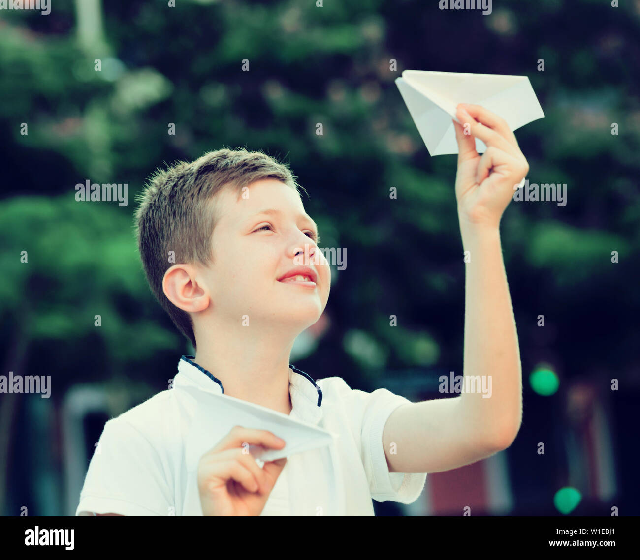 portrait of glad boy throwing paper airplanes in park on summer day ...