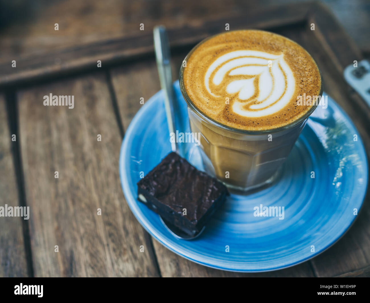 Piccolo Latte coffee topping with flower art from milk in small glass with  a piece of homemade brownies cake on blue ceramic plate on wooden tray on w  Stock Photo - Alamy