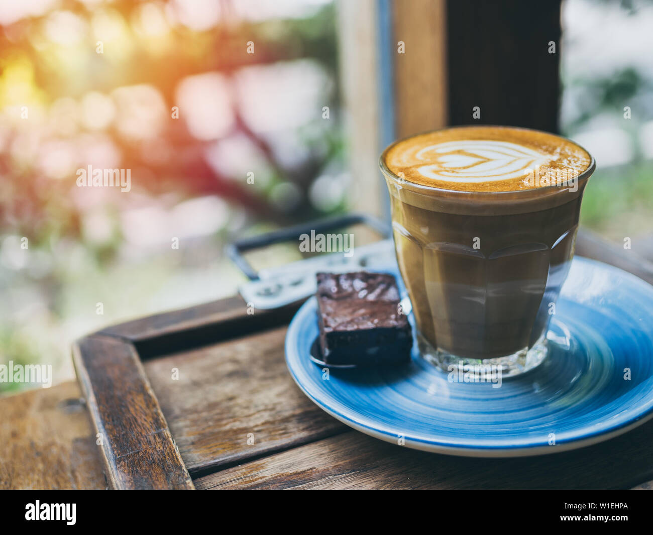 https://c8.alamy.com/comp/W1EHPA/piccolo-latte-coffee-topping-with-flower-art-from-milk-in-small-glass-with-a-piece-of-homemade-brownies-cake-on-blue-ceramic-plate-on-wooden-tray-on-w-W1EHPA.jpg
