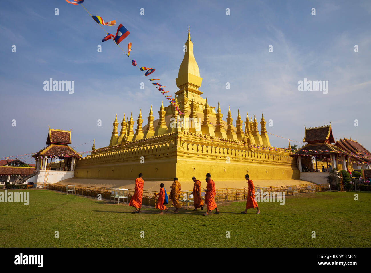 The golden Buddhist stupa of Pha That Luang with Buddhist monks walking below, Vientiane, Laos, Indochina, Southeast Asia, Asia Stock Photo