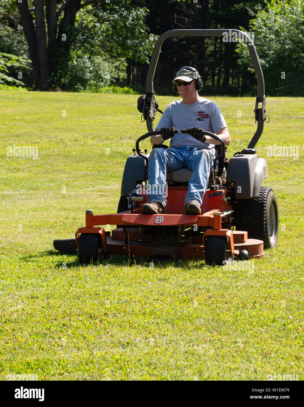 A male worker mowing a lawn with a commercial lawn mower in Speculator, NY USA Stock Photo