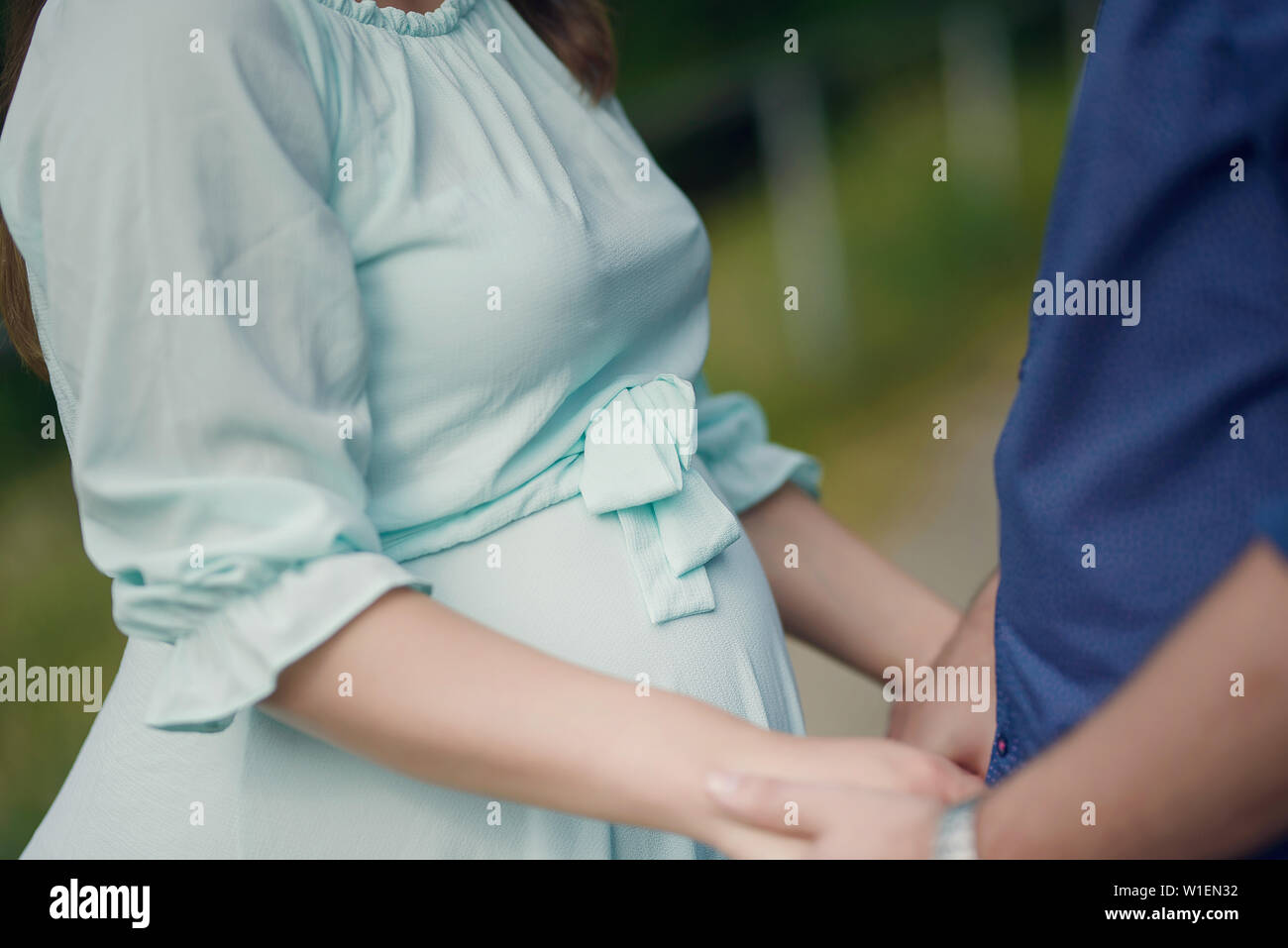 Cropped shot of handsome Caucasian couple holding hands with focus on the pregnant woman's beautiful round tummy, concept for happy family expecting Stock Photo