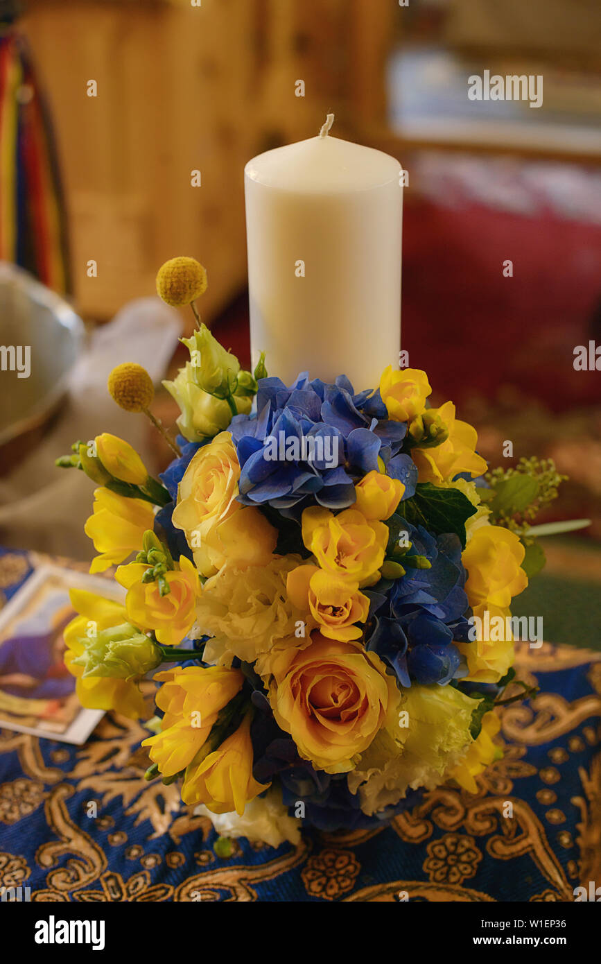 Baptismal candle decorated with a yellow spring flowers bouquet in preparation for the baptism, first of seven Sacraments in the Orthodox Church Stock Photo
