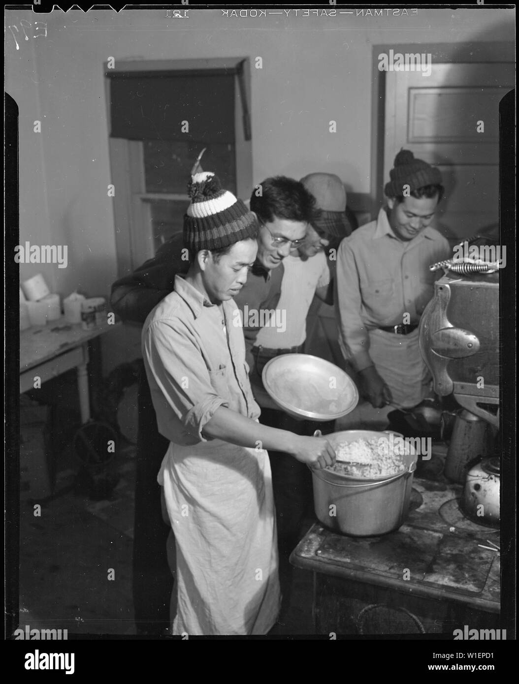 Heart Mountain Relocation Center, Heart Mountain, Wyoming. Hungry beet workers look over the should . . .; Scope and content:  The full caption for this photograph reads: Heart Mountain Relocation Center, Heart Mountain, Wyoming. Hungry beet workers look over the shoulder of the Chef for the day as he prepares the evening meal. These Nisei boys are members of a crew of volunteer beet workers who helped in the harvest of sugar beets near Billings Montana. Stock Photo